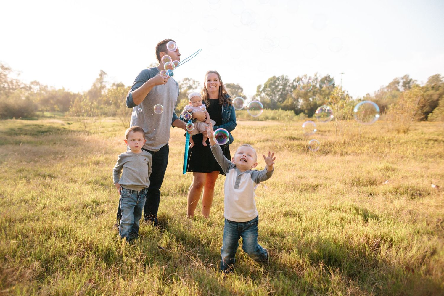 family playing with bubbles in a field at golden hour