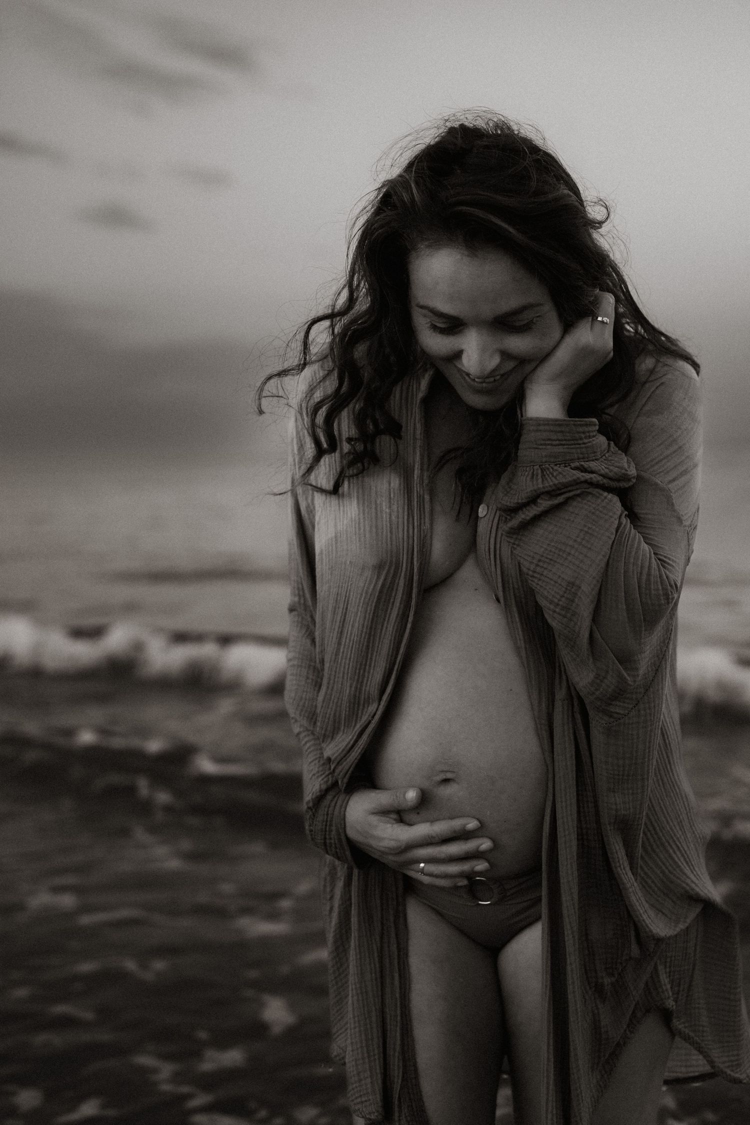Pregnant woman at the beach in Denia holding her belly - Denia maternity photographer
