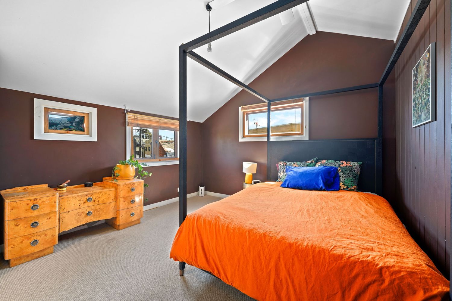 Modern bedroom with sloped ceiling features dark brown walls, orange bedding, and matching wooden dressers.