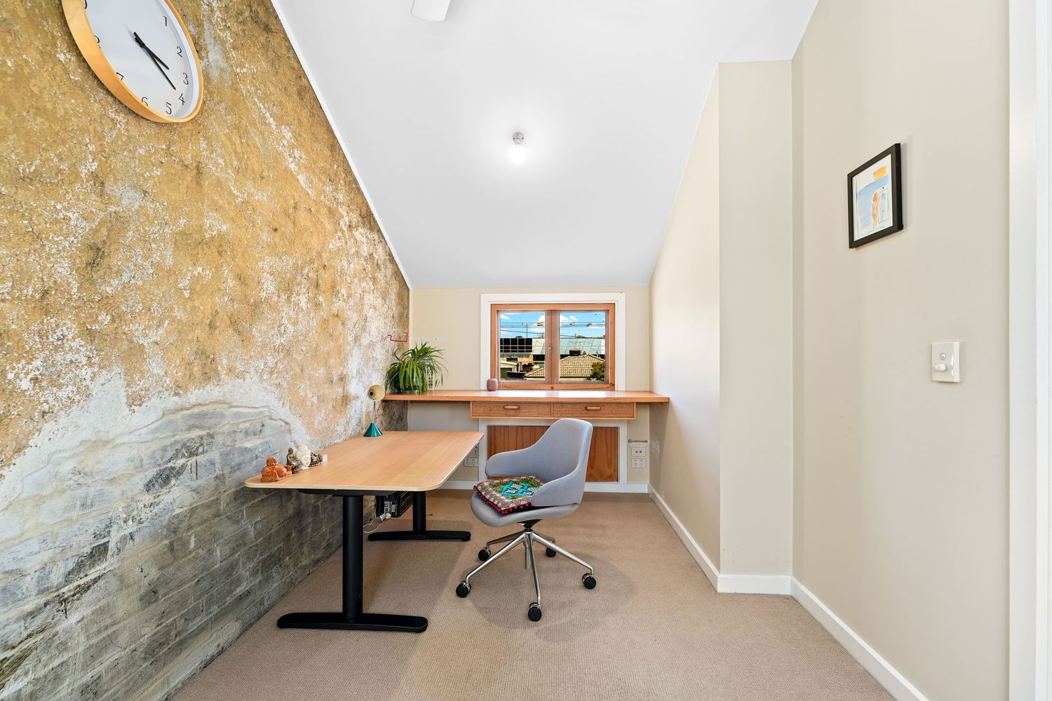 Modern home office nook with exposed rock wall, standing desk, ergonomic chair and window view.