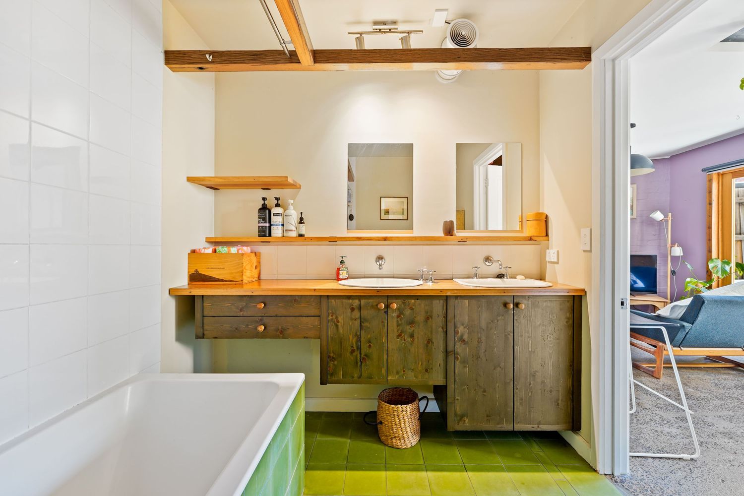 Modern bathroom interior with lime green flooring, rustic wooden vanity, and white bathtub next to glass door.