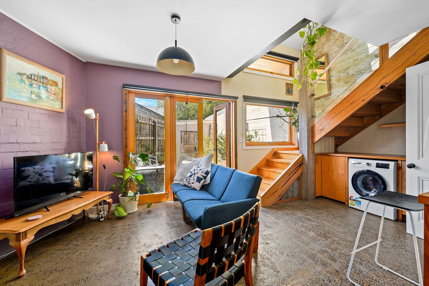 Cozy living room with purple walls, blue sofa, wooden TV stand, and spiral staircase leading upstairs.