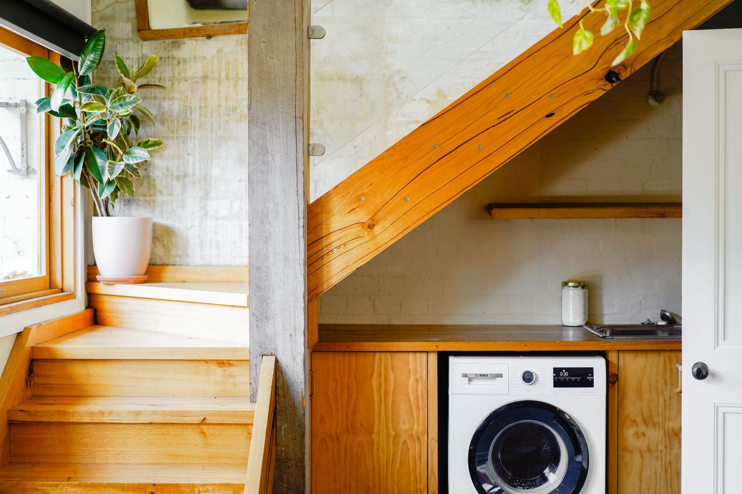 Wooden staircase with integrated washing machine storage underneath in a minimalist home interior.