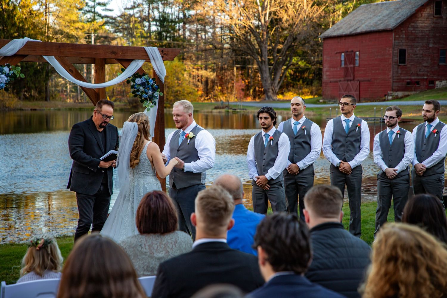 A beautiful outdoor autumn wedding scene showing a young flower girl in a white dress holding a bouquet of flowers.