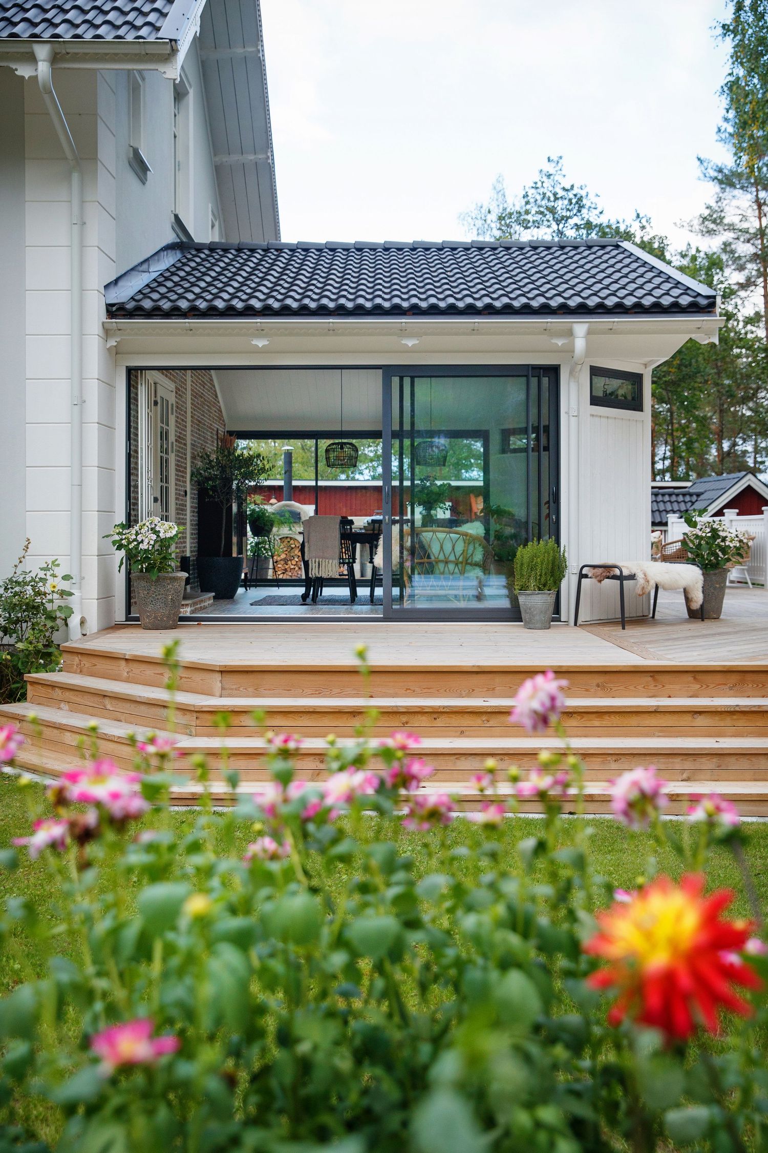 Contemporary white house exterior with large glass windows and a wooden deck surrounded by colorful flowers.