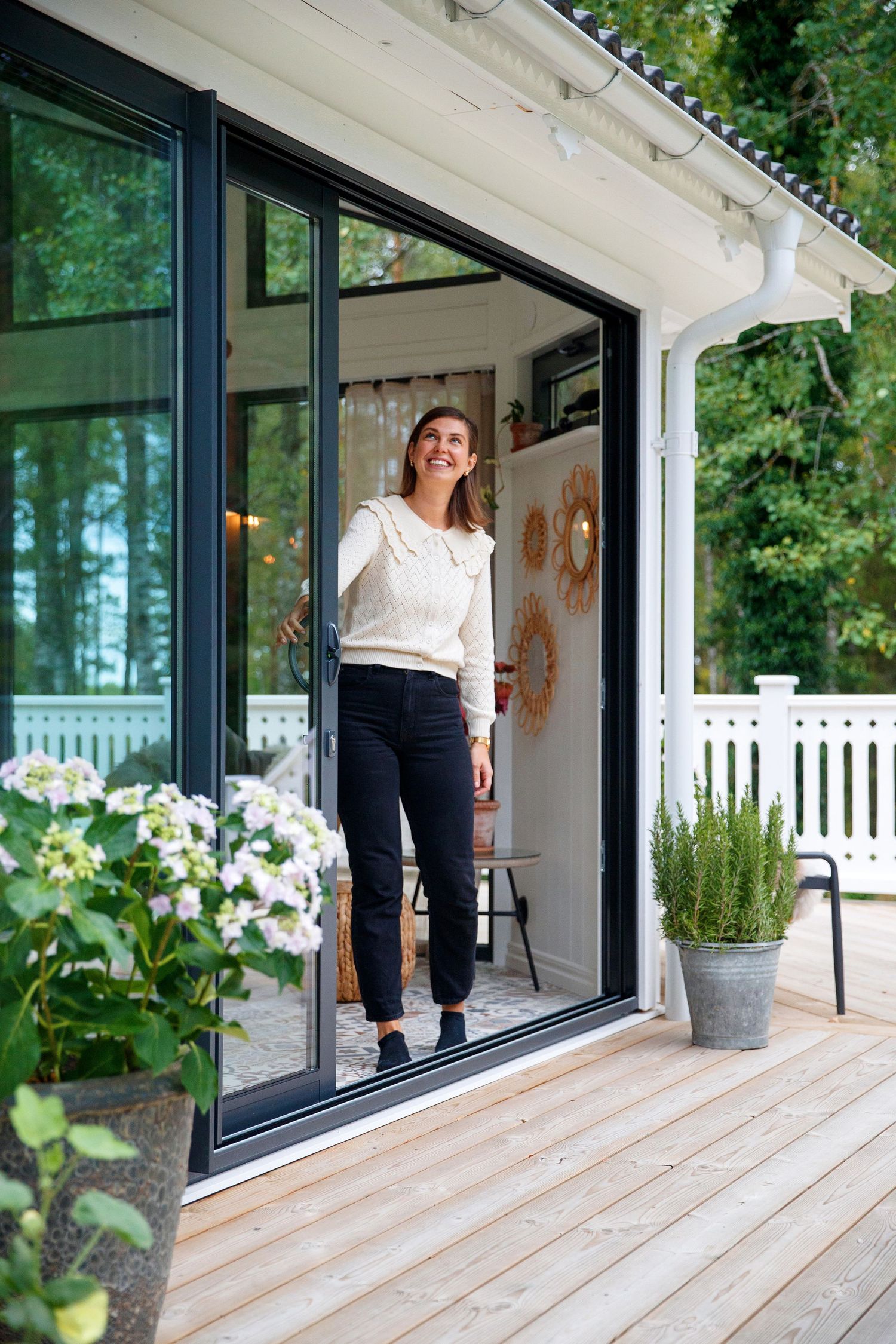 Light-filled patio with wooden decking and floor-to-ceiling windows surrounded by lush greenery.