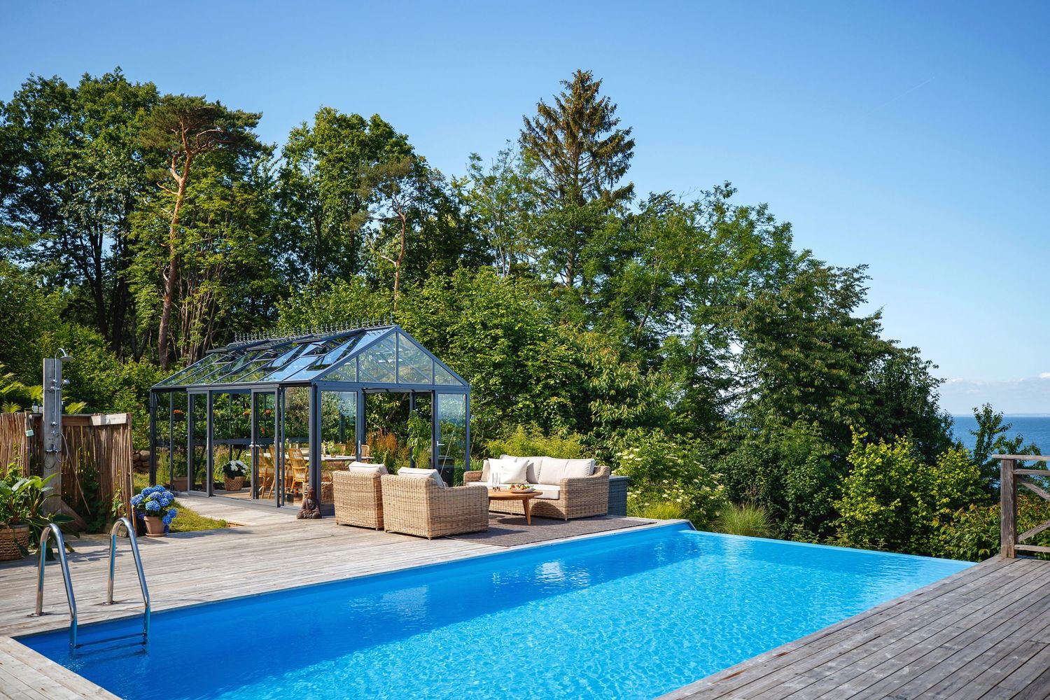 Luxurious infinity pool and greenhouse surrounded by trees overlooking a scenic landscape.