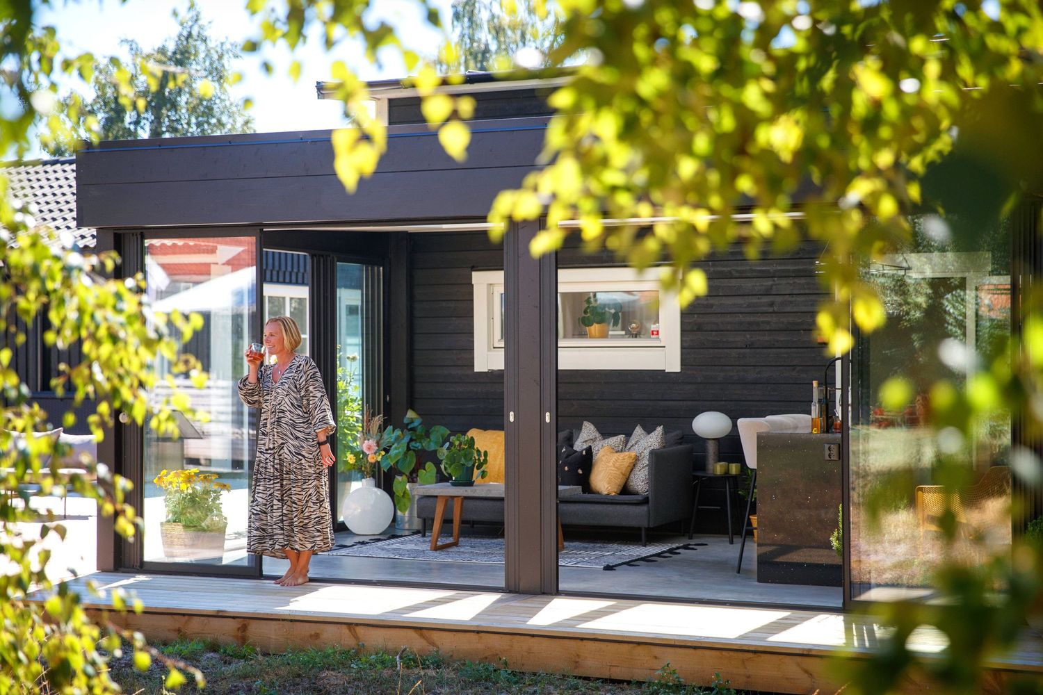 Modern house exterior viewed through natural foliage with large windows and clean architectural lines.
