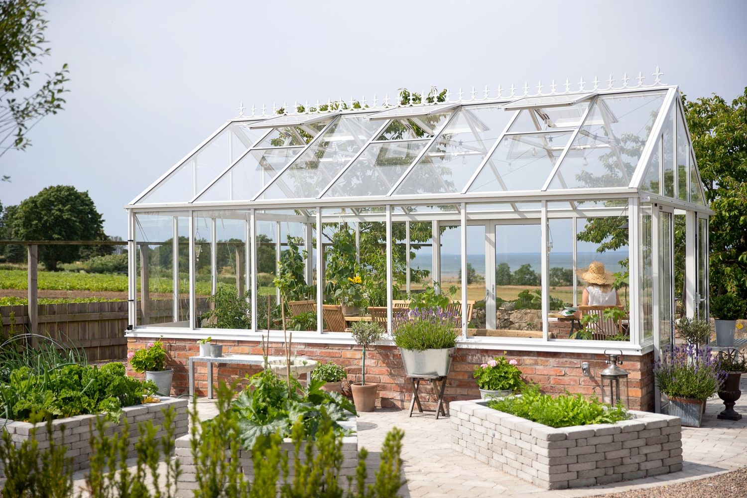 Traditional glass greenhouse with brick base surrounded by manicured garden beds.