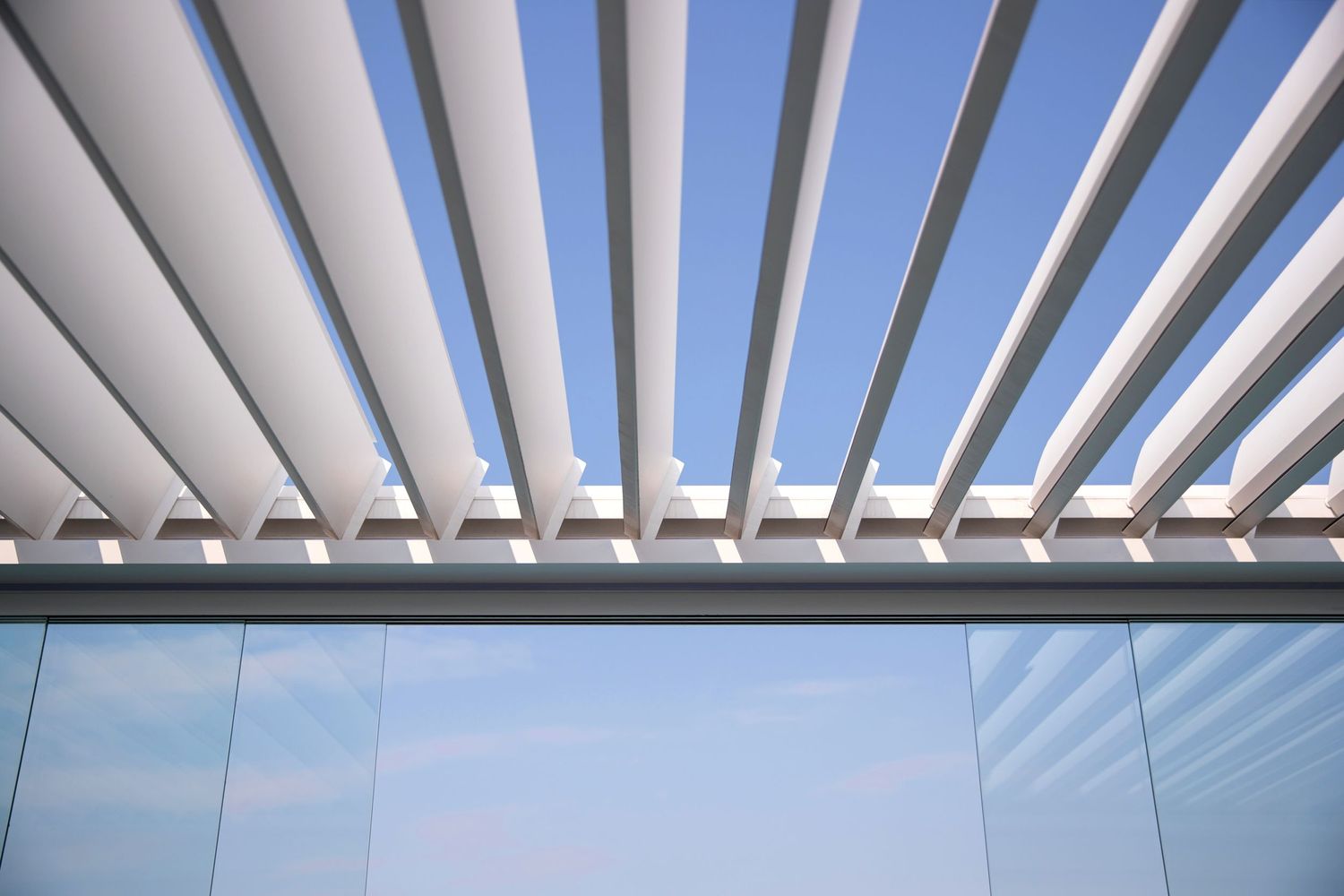 Modern white pergola slats against blue sky creating geometric pattern.