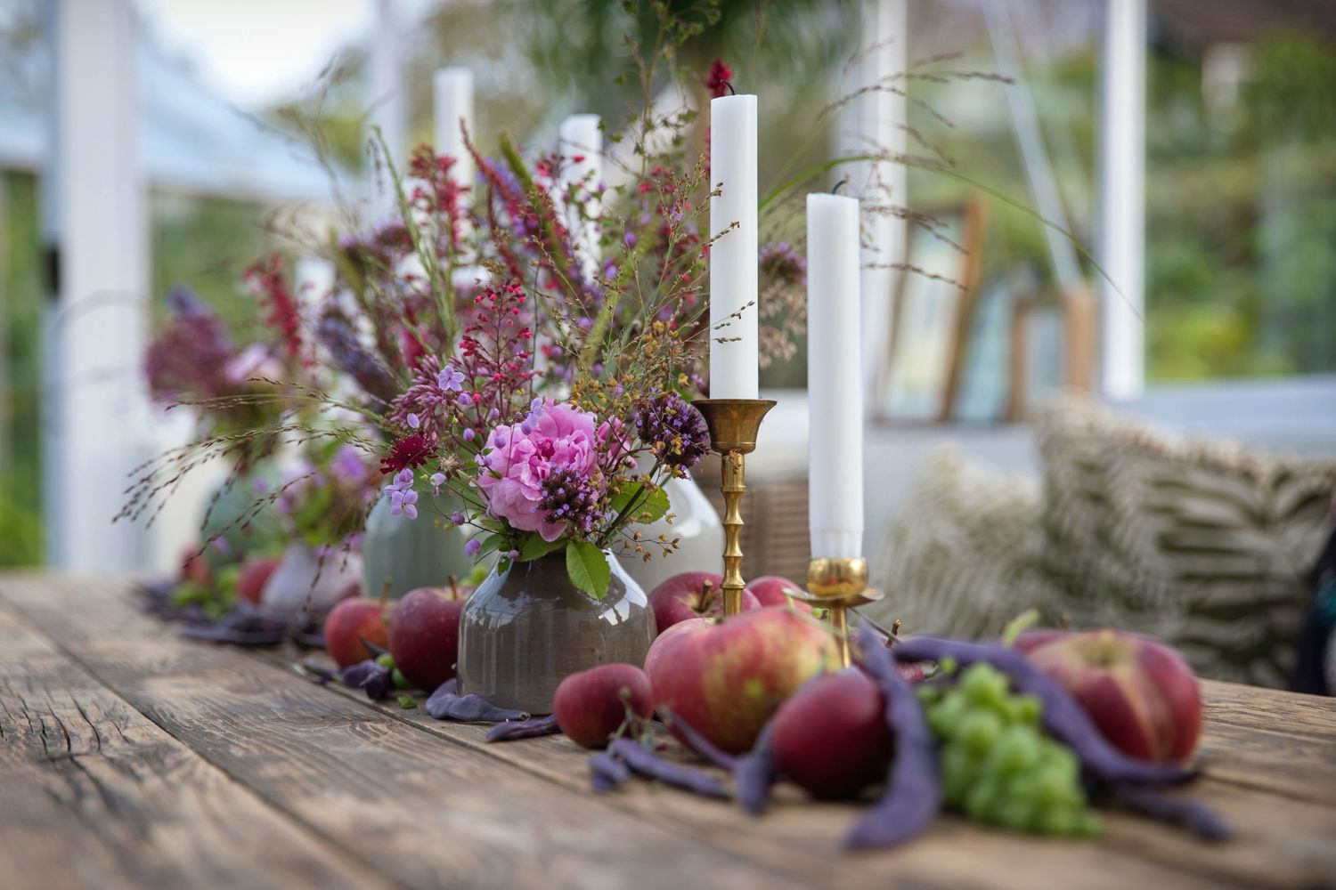 Rustic wooden table decorated with fresh flowers, candles and autumn fruits.