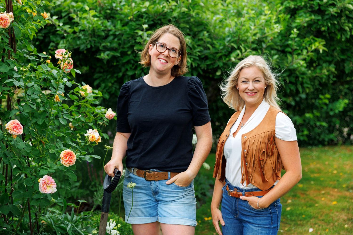 Two friends standing together in garden with blooming roses.