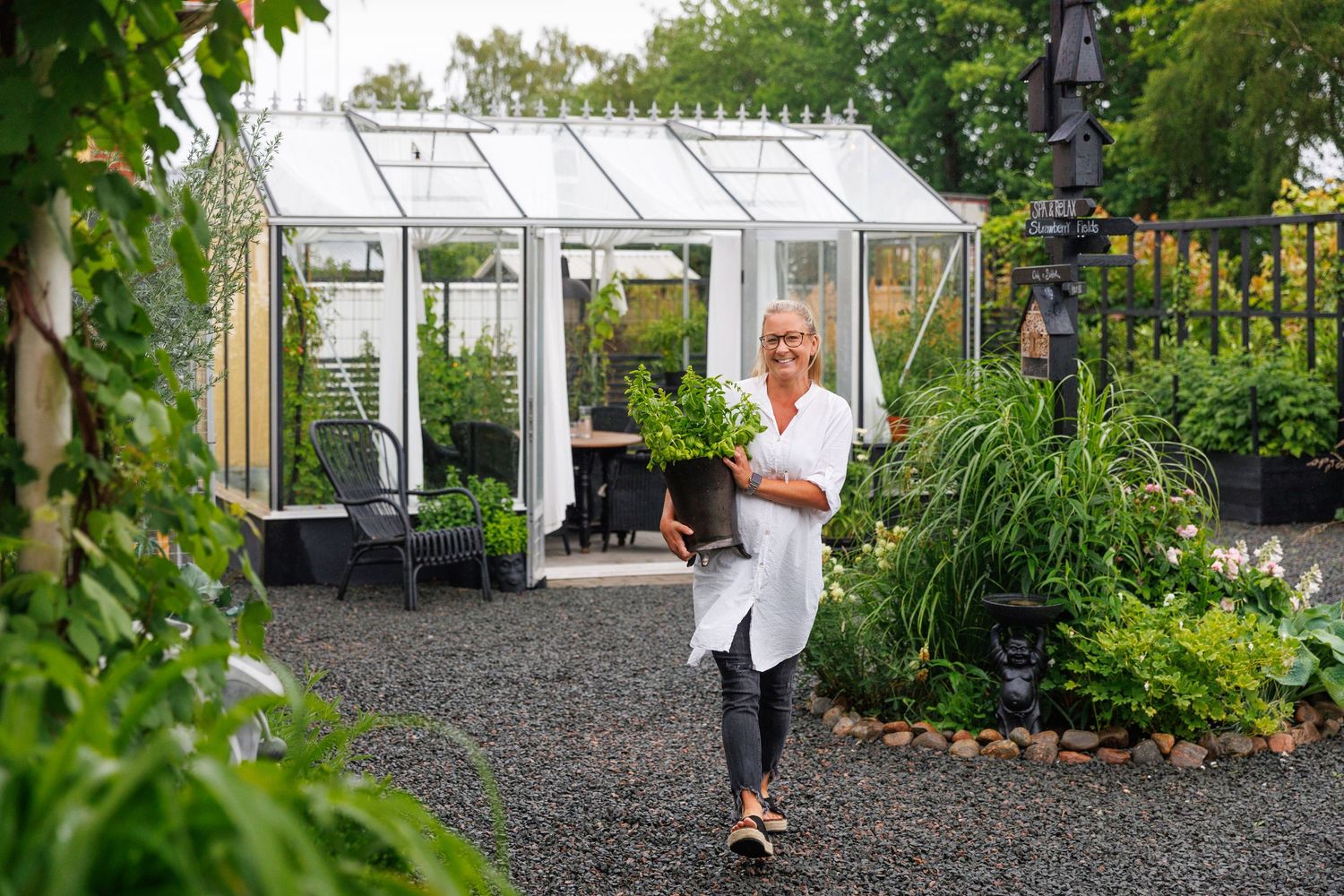 Glass greenhouse with plants visible in well-maintained garden setting.