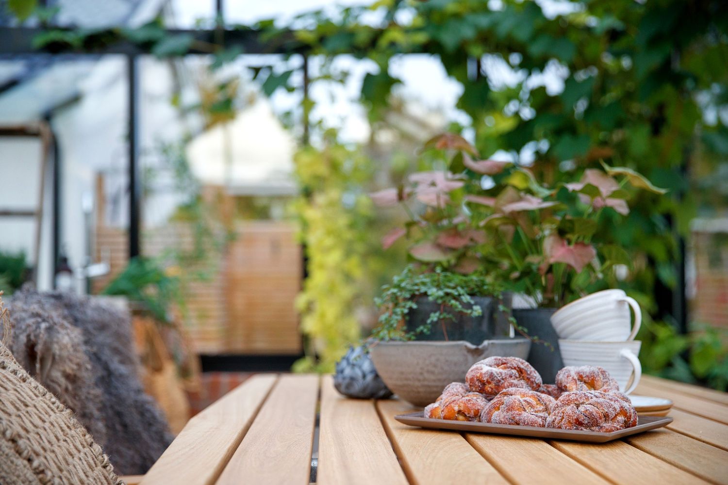 Outdoor garden table setting with cups and pastries in a serene environment.