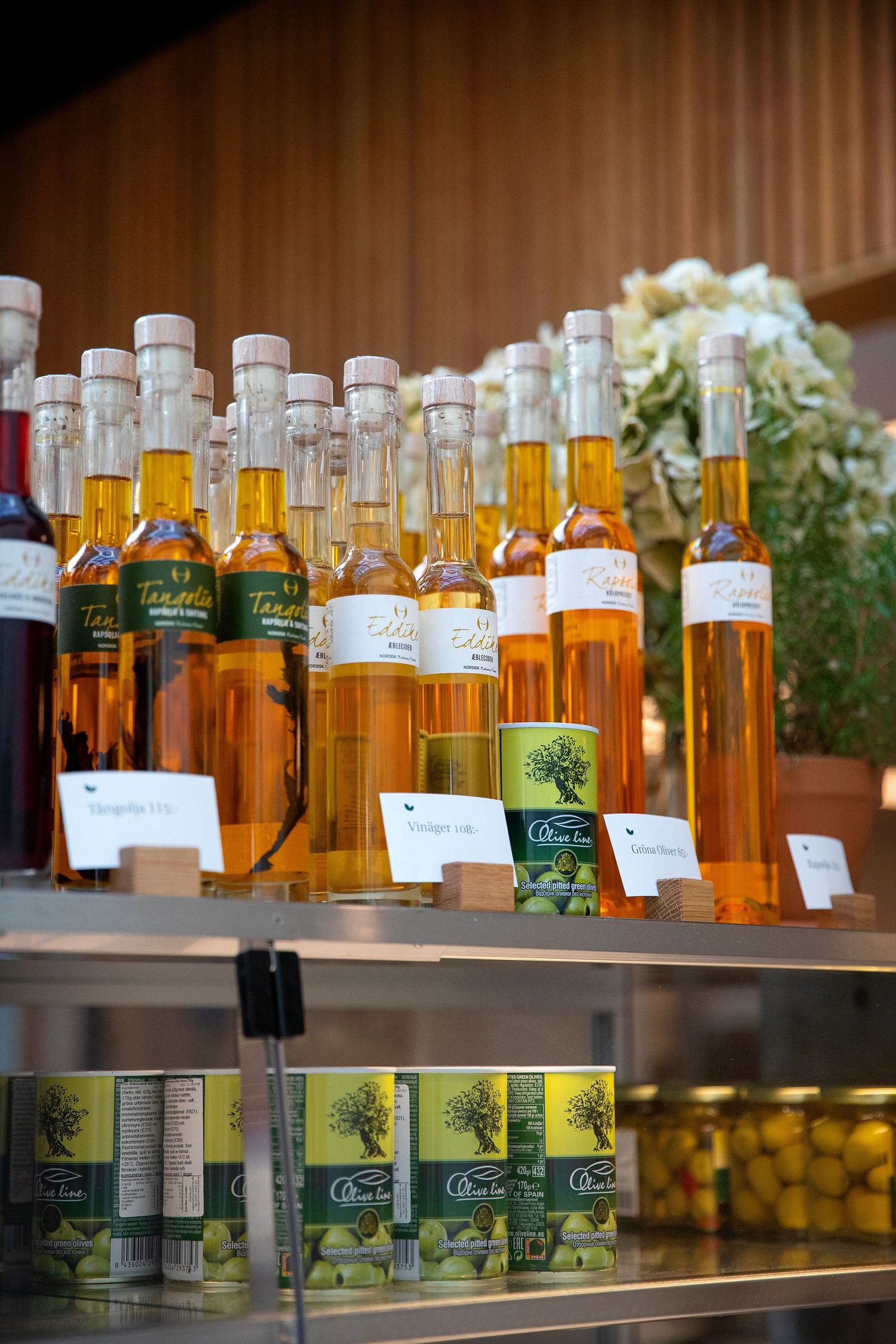 Rows of amber-colored bottled olive oils displayed on wooden shelves.