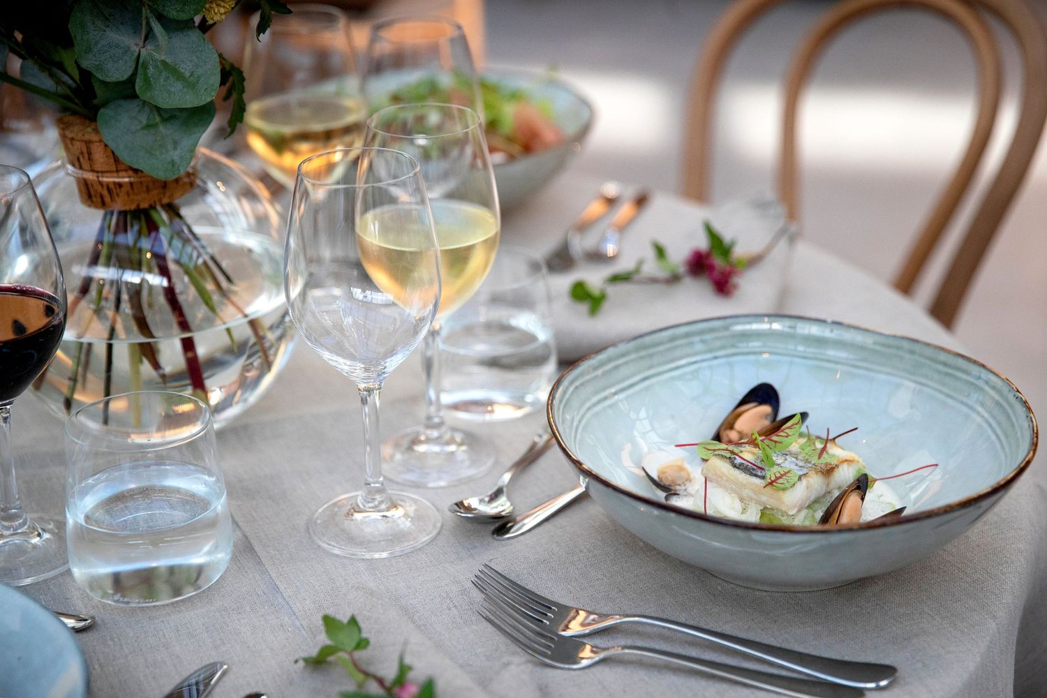 Elegant table setting with wine glasses, blue ceramic plate, and gourmet meal.