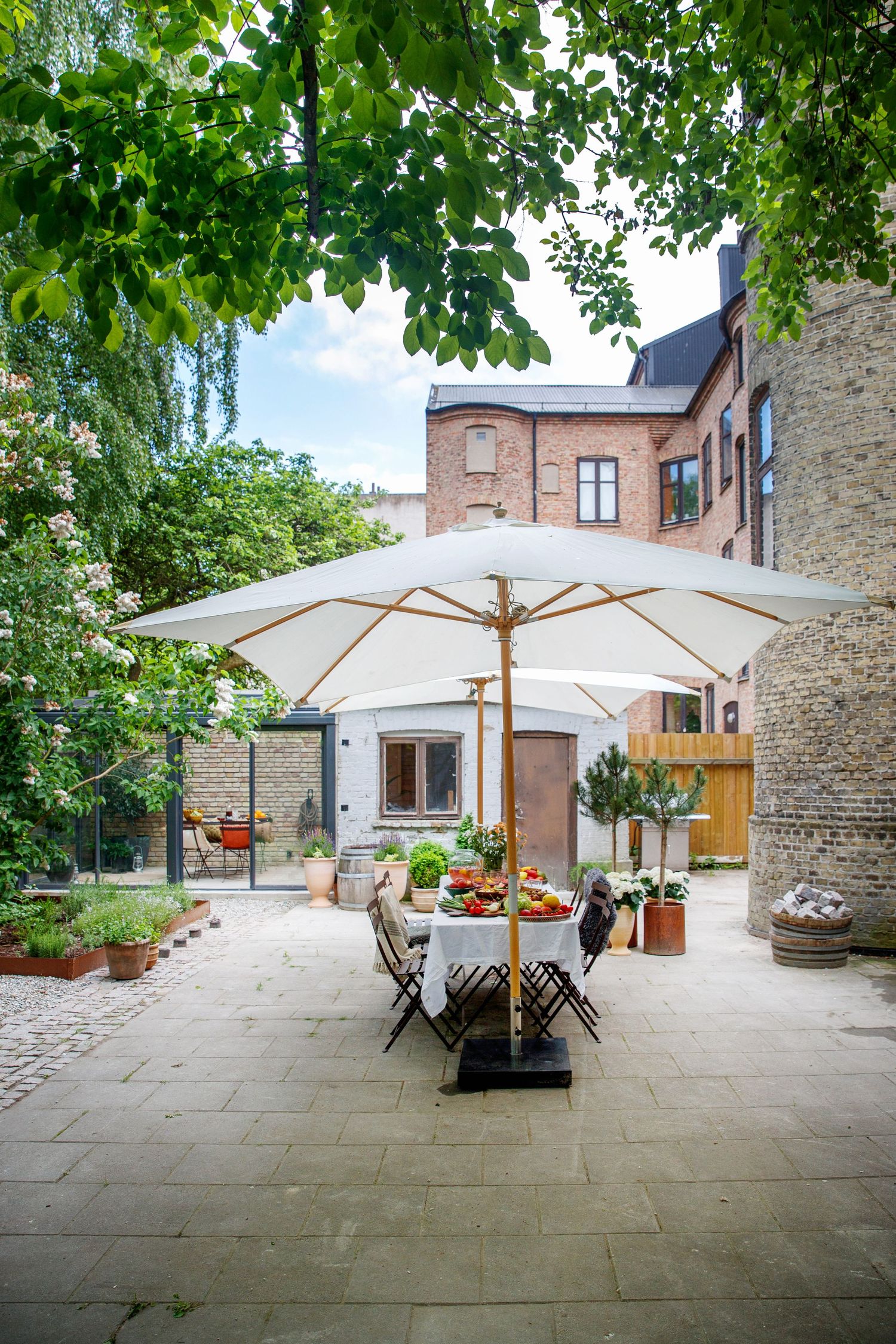 Stone courtyard with white umbrellas and outdoor dining furniture creating an elegant entertaining space.
