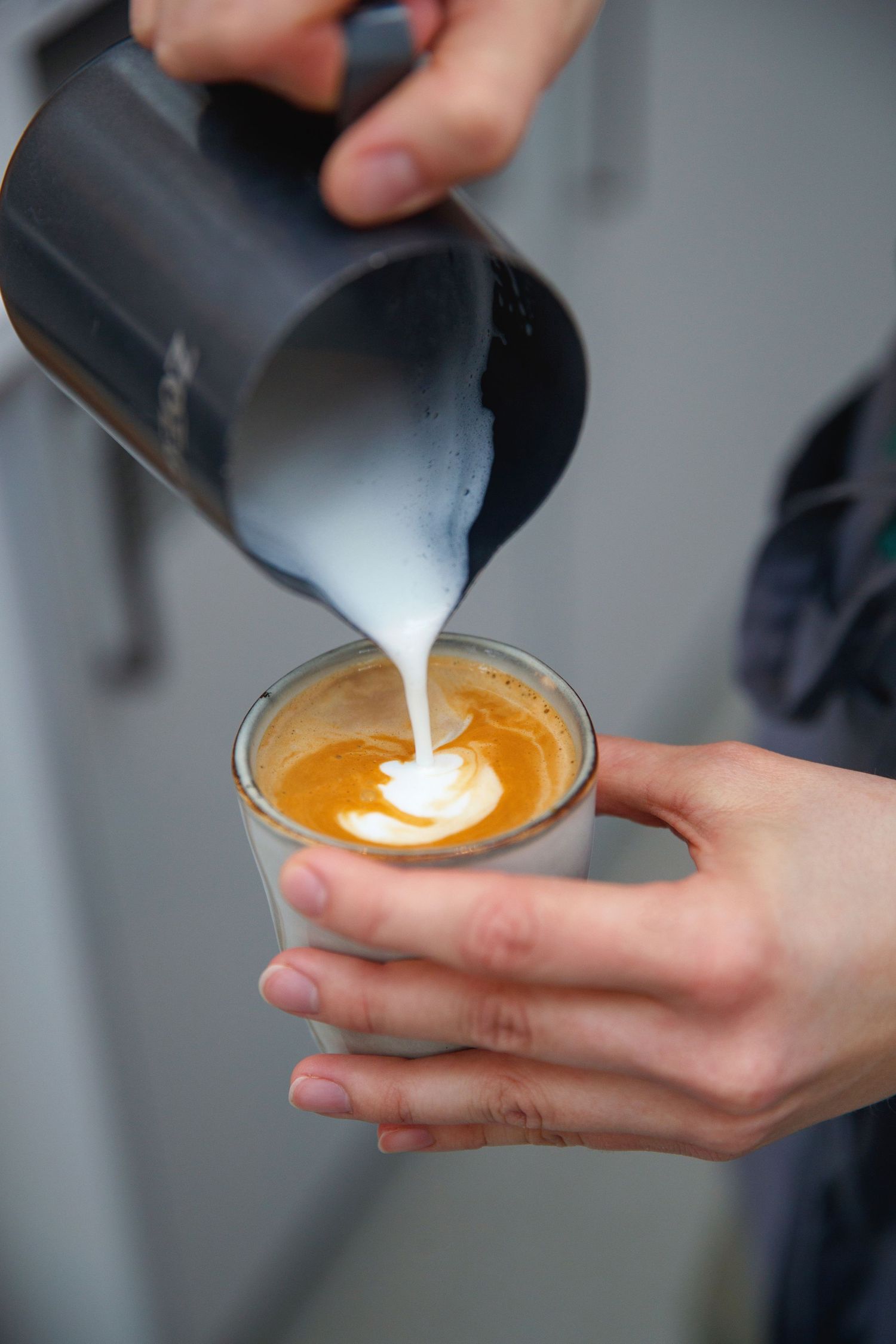 Barista pouring steamed milk into coffee to create latte art pattern.