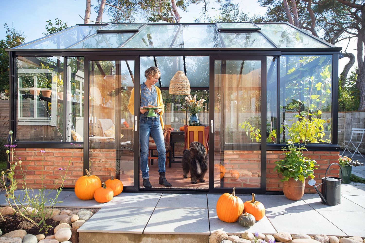 Modern glass greenhouse with orange pumpkins decorating the entrance and plants inside.