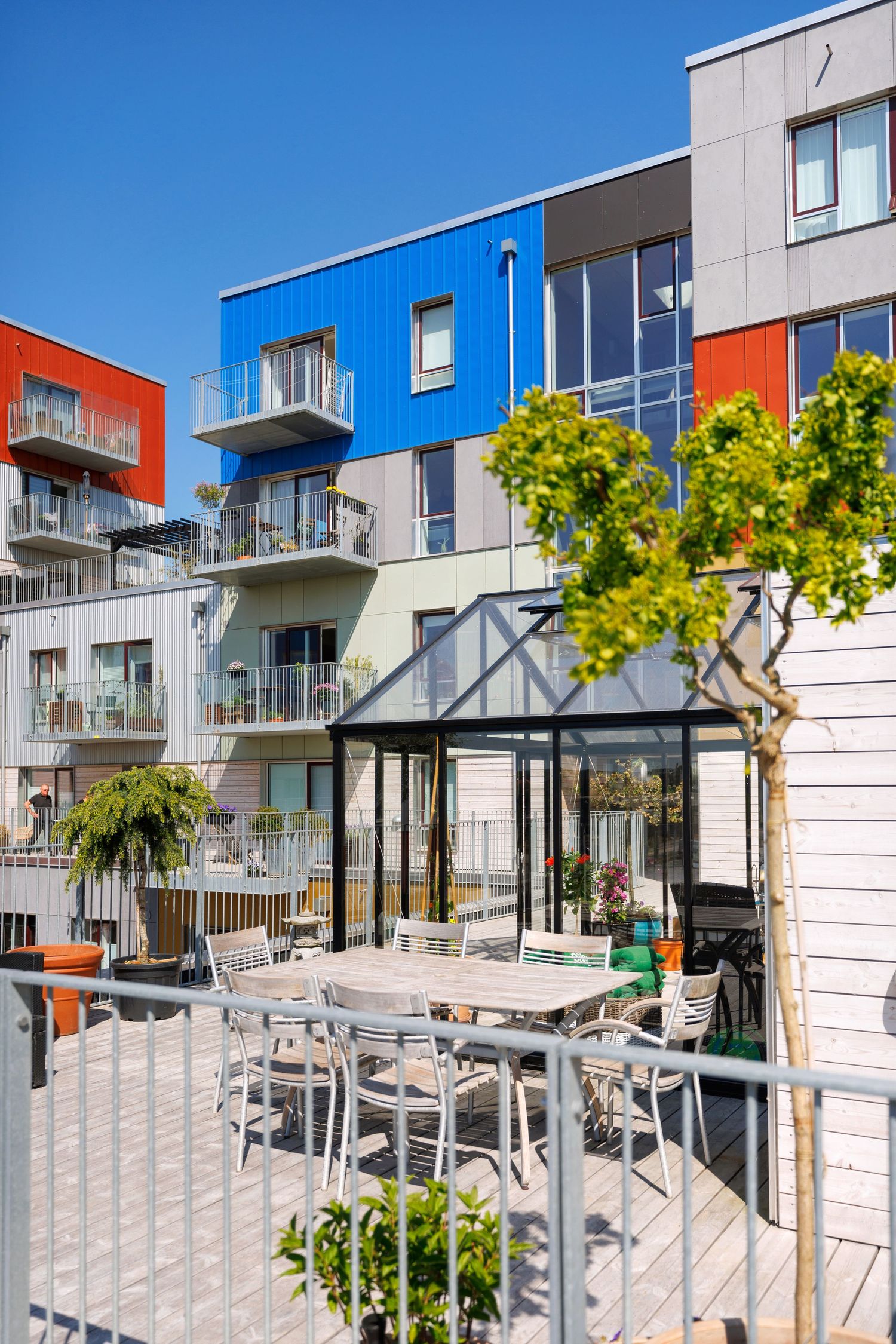 Modern apartment building with blue and orange accents featuring outdoor dining area.