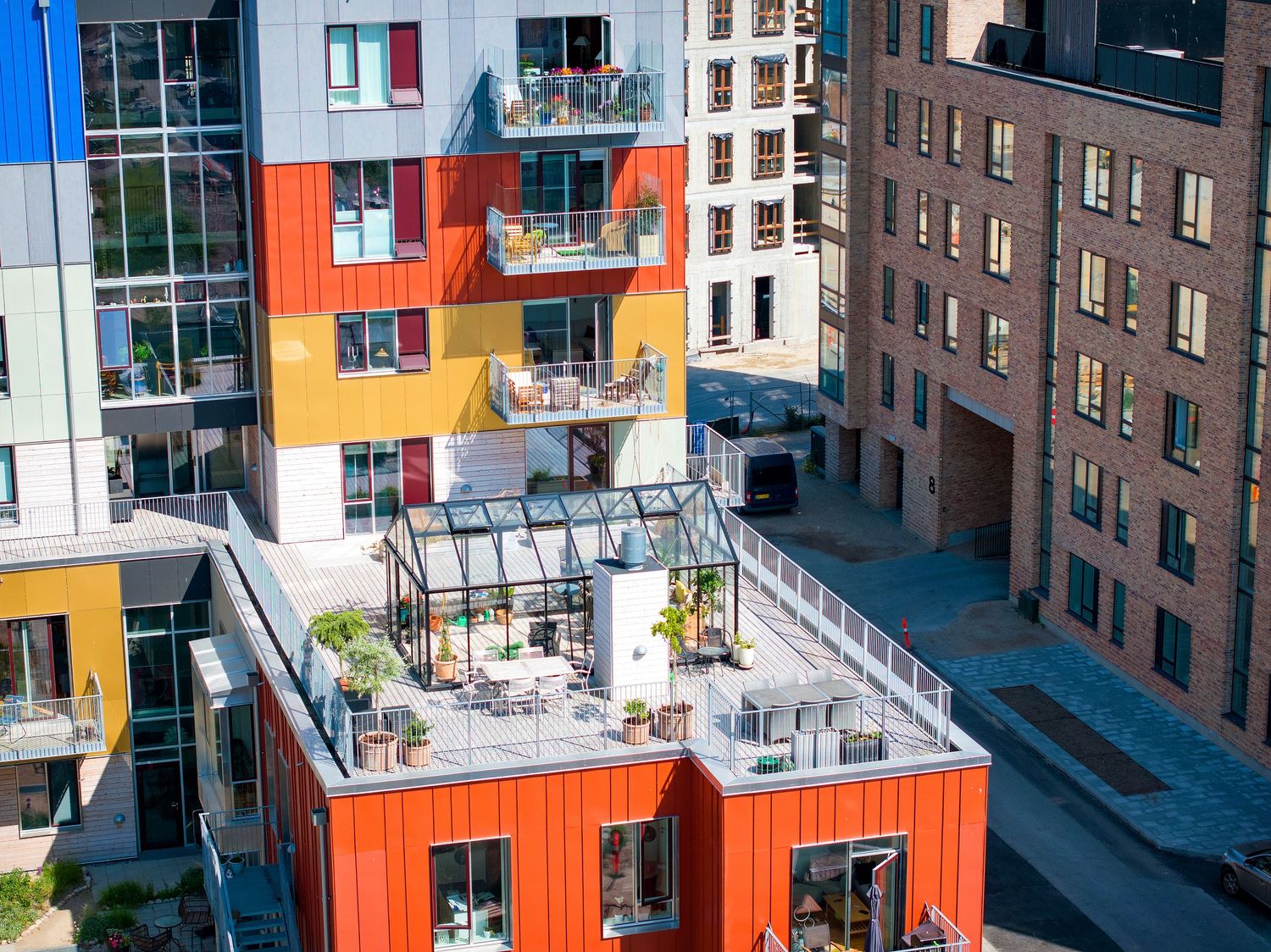 Modern apartment building with colorful orange and yellow facade and rooftop terrace with greenhouse.