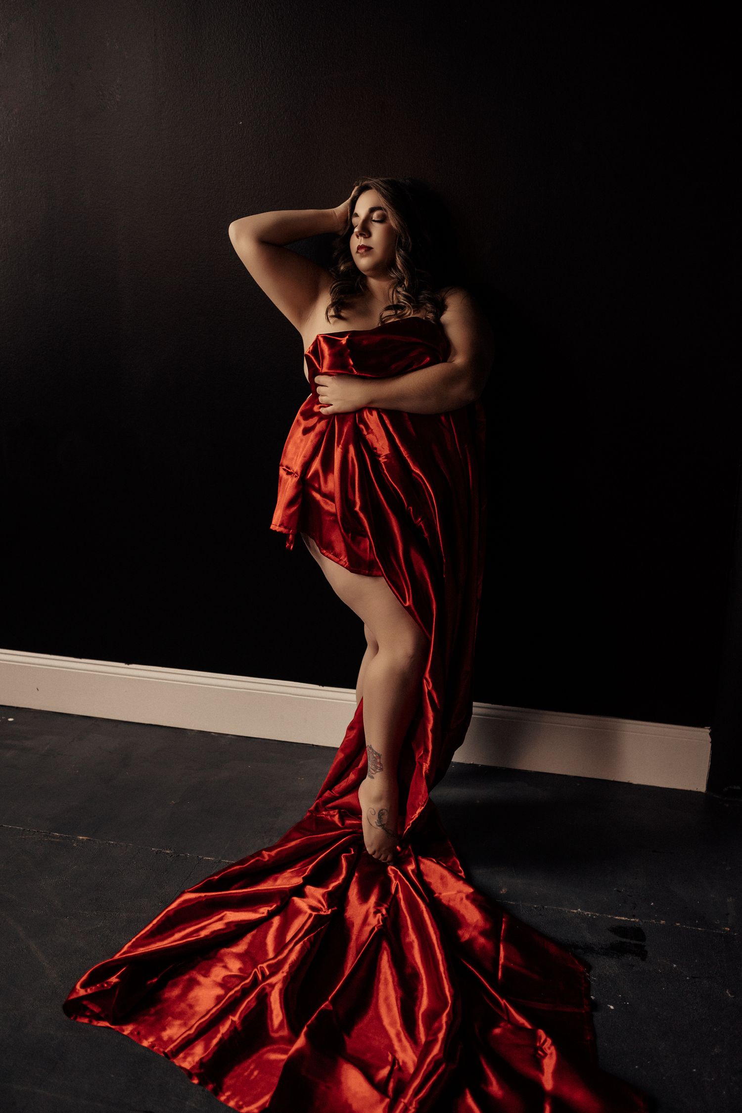 Dramatic portrait in a flowing red satin gown against dark background.