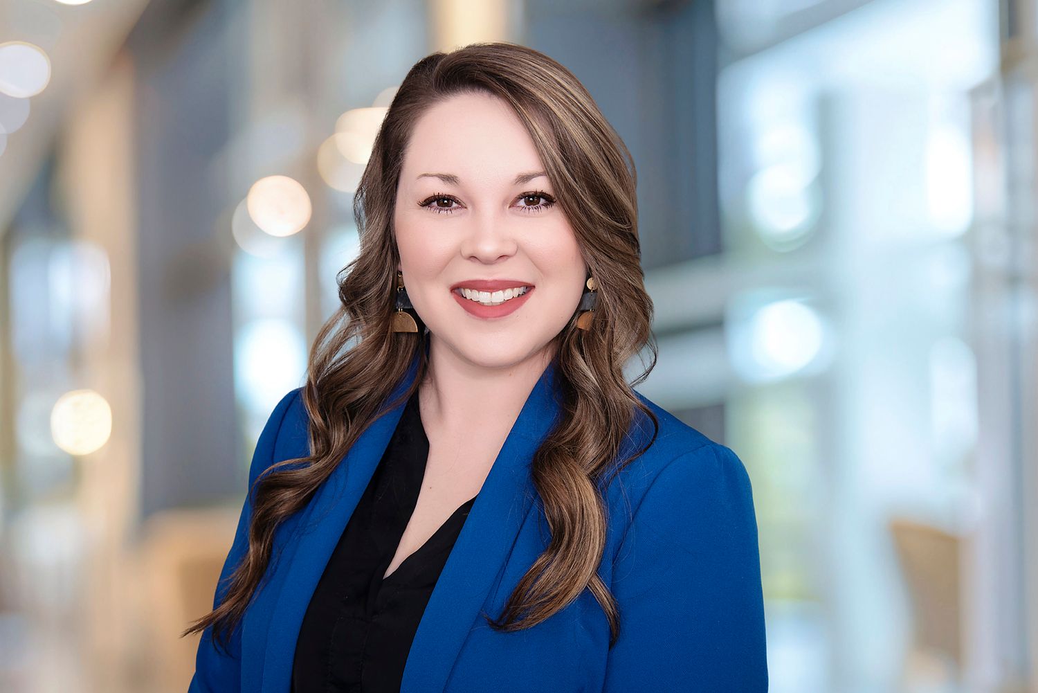 Professional headshot with bright blue blazer against blurred office background with bokeh lights.