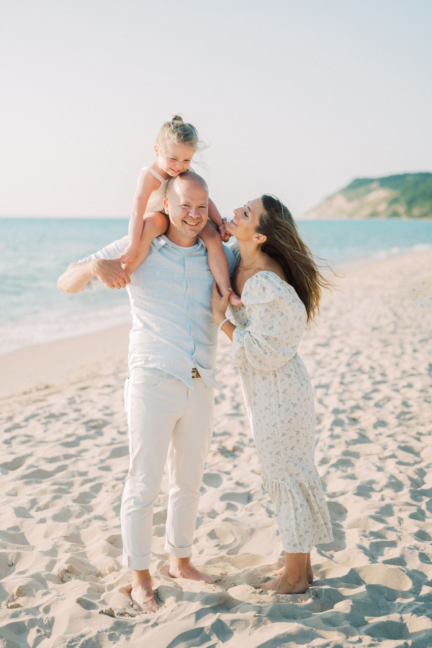 A couple and child playing together on a sunny beach with cliffs in the background.