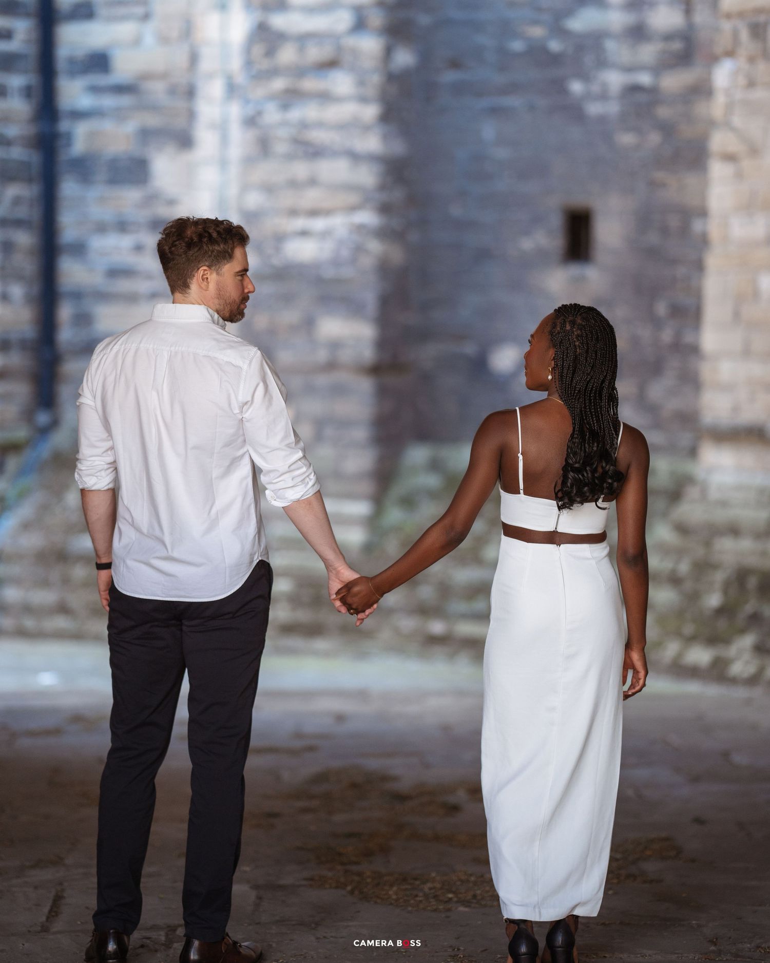 A romantic wedding photo series showing a couple in formal attire walking hand in hand against a rustic stone wall backdrop.