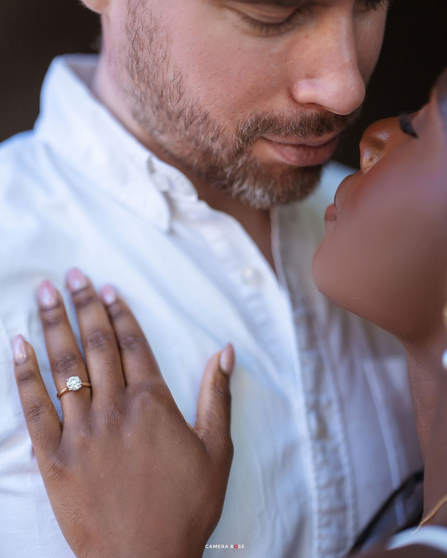 Close up of hands showing off an engagement ring in a romantic pose against a white fabric background.