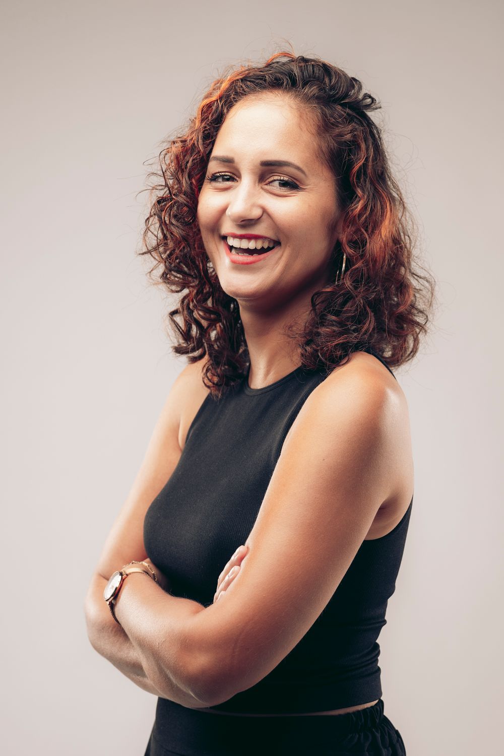 Portrait of a person with curly hair wearing black sleeveless top against light background.