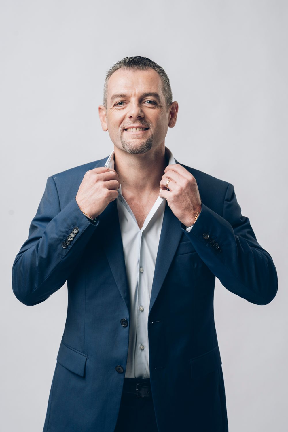 Professional in navy suit adjusting collar against light background.