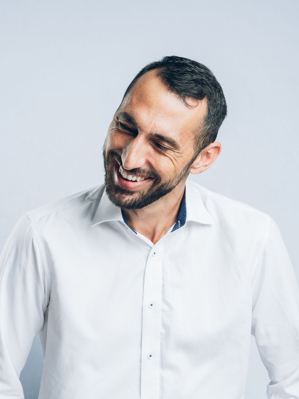 A person in a crisp white button-down shirt laughs joyfully against a light background.