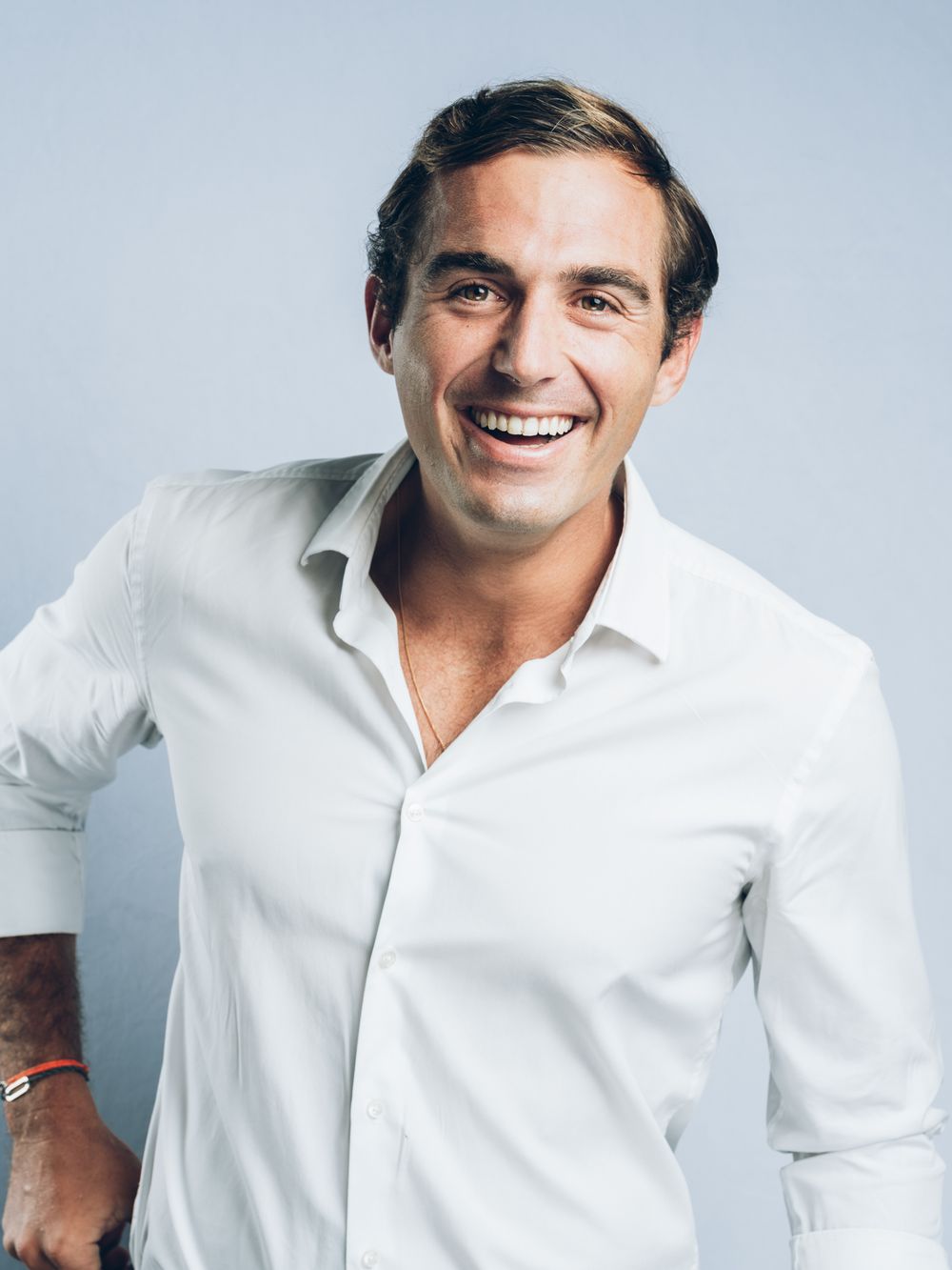 Professional portrait of someone wearing a crisp white button-down shirt smiling against a light gray background.