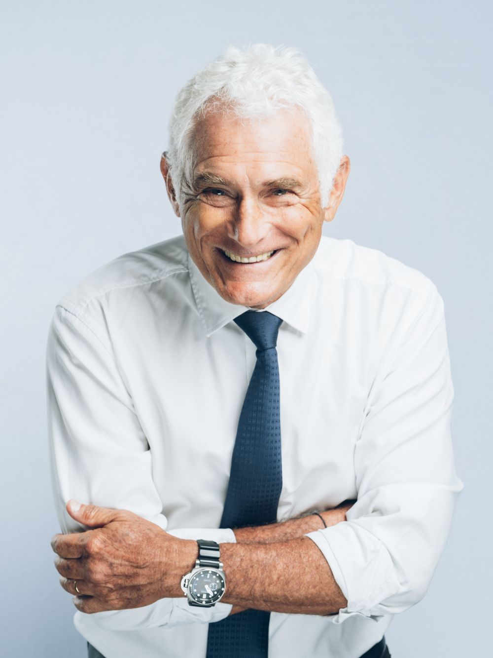 Cheerful older professional in white dress shirt and blue tie shown in four candid poses against light blue background.