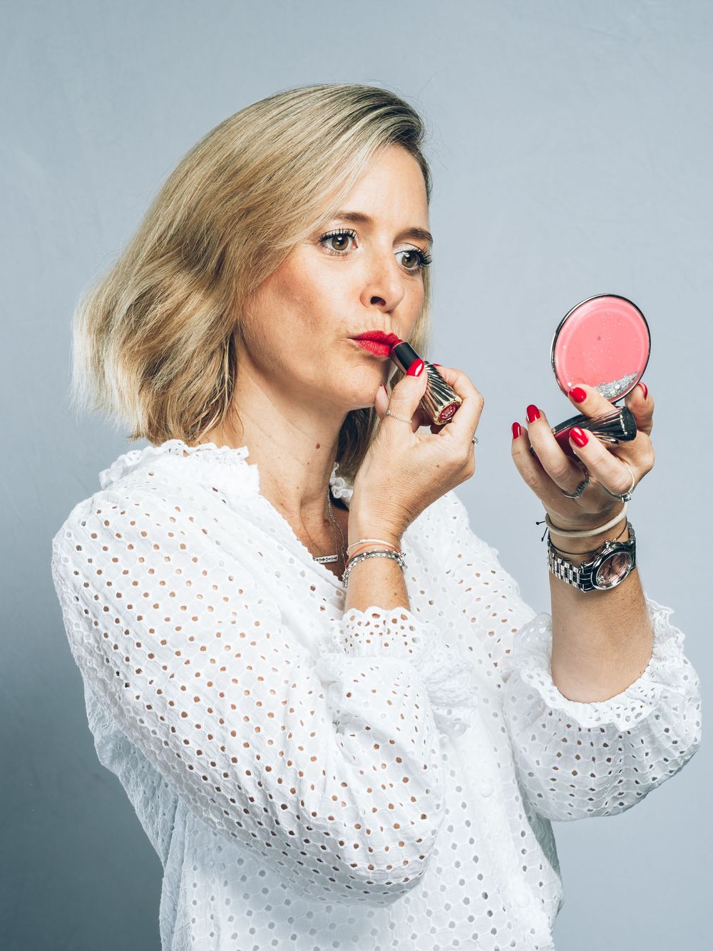 Someone wearing a white polkadot blouse applies lipstick while looking in a handheld mirror in a series of poses.