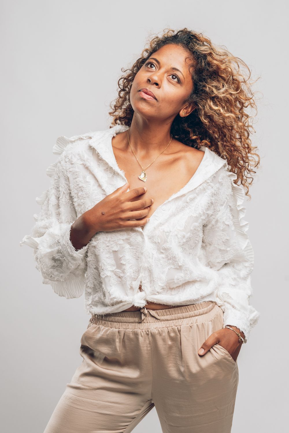 Fashion model in white ruffled blouse and beige pants against light background.