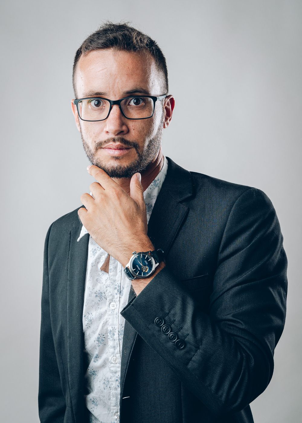 Professional headshot of someone in glasses and suit jacket with hand thoughtfully on chin.