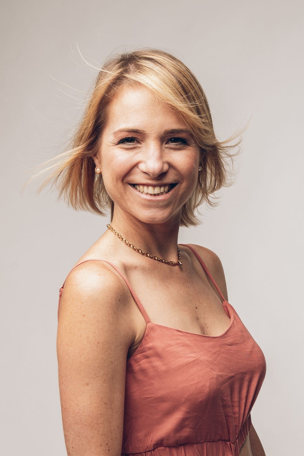 Portrait of a person in a coral tank top with short blonde hair smiling warmly.