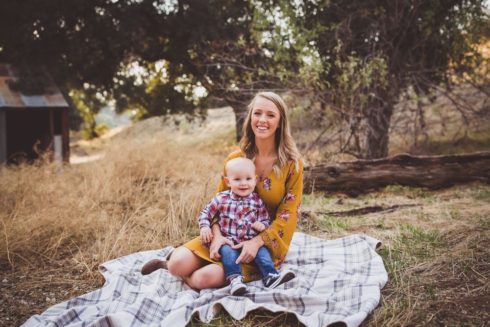 Family wearing coordinated outfits sits together on white blanket for outdoor autumn photoshoot in nature setting.