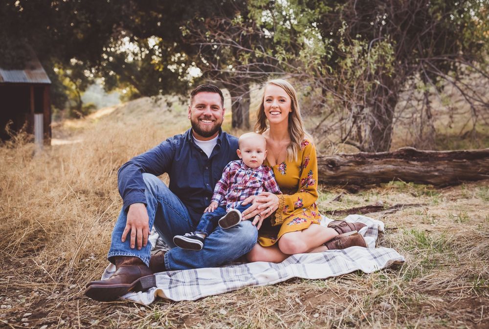 Family group relaxes on a blanket during an outdoor autumn photo session in a golden natural setting.