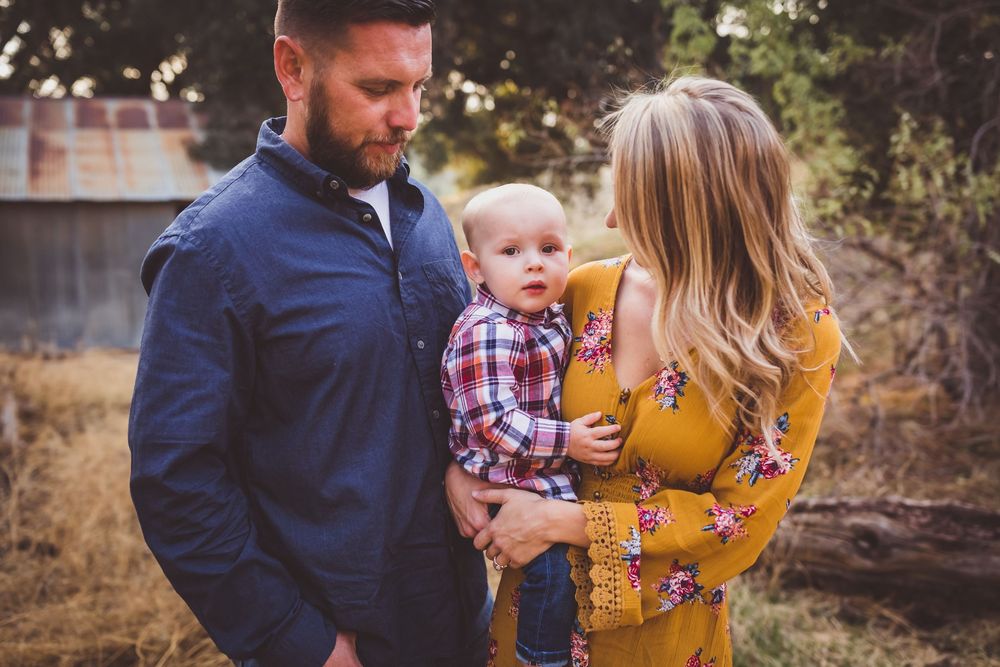 Family wearing fall colors poses together in outdoor setting with autumn grass and natural lighting.