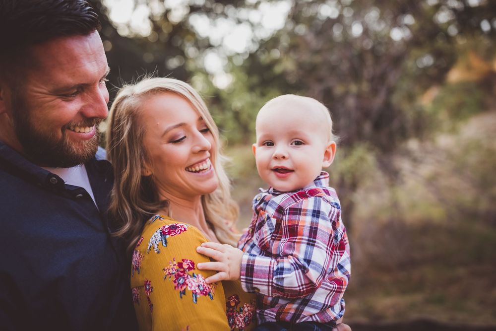 A family laughs together outdoors wearing coordinated fall outfits including a yellow dress and plaid shirt.