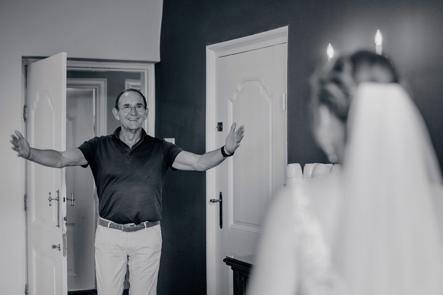 Black and white photo of someone standing in a doorway with their arms outstretched while being photographed.