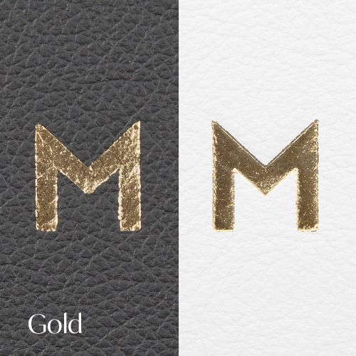 Letter M in metallic gold foil shown on contrasting leather and white backgrounds.