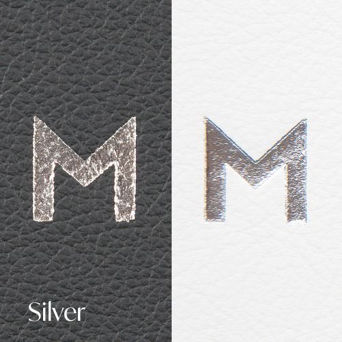 Letter M logo rendered in metallic silver finish on black leather texture with light background comparison.
