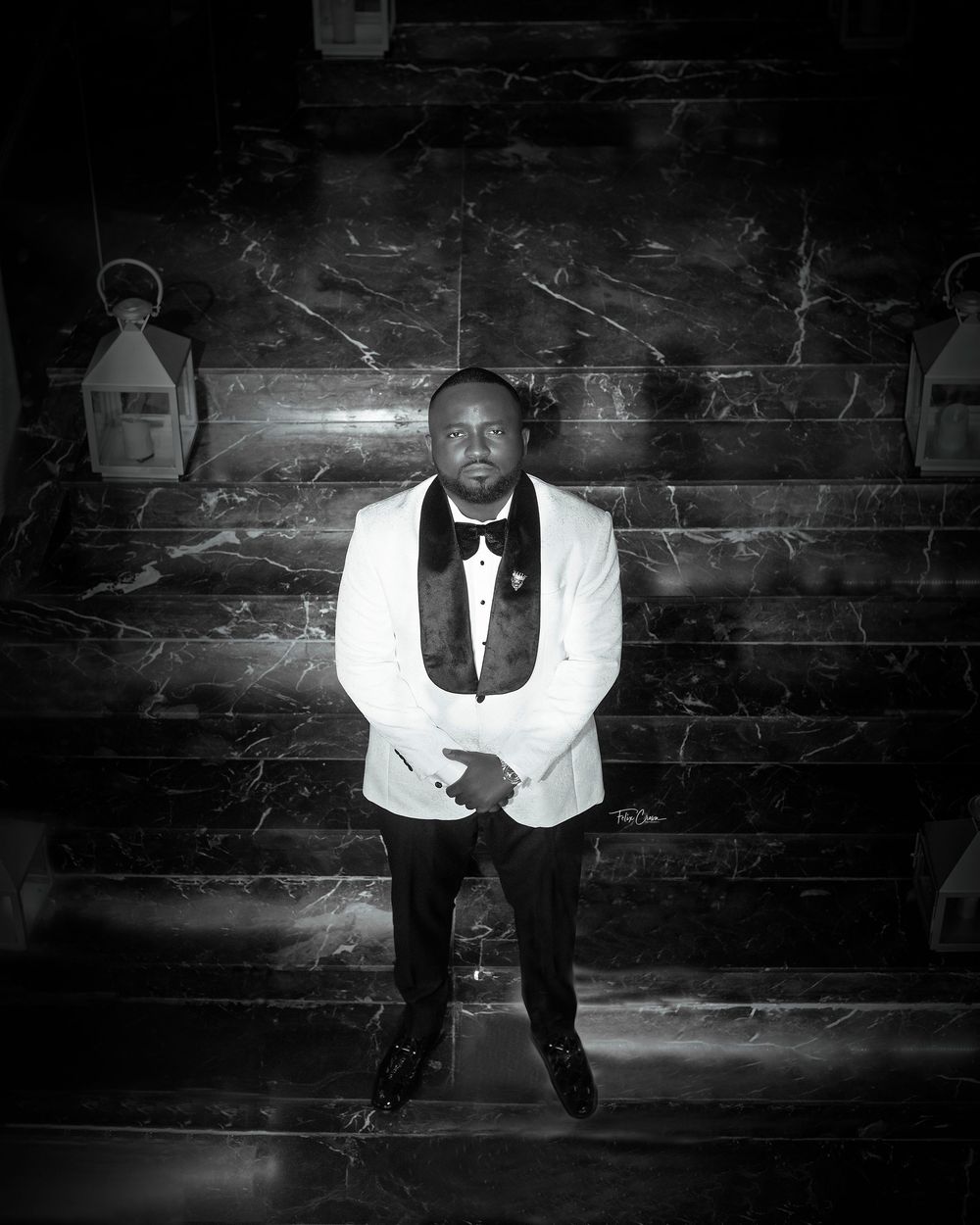 Black and white portraits show groom in classic tuxedo sitting on rustic wooden steps.