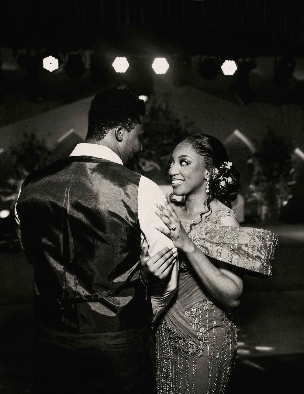 A couple shares an intimate dance moment under hexagonal lights in black and white photography.