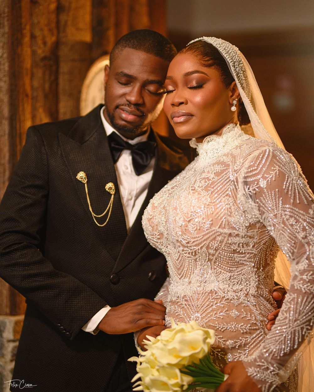 A loving couple share an intimate moment on their wedding day wearing elegant black tuxedo and white lace gown.