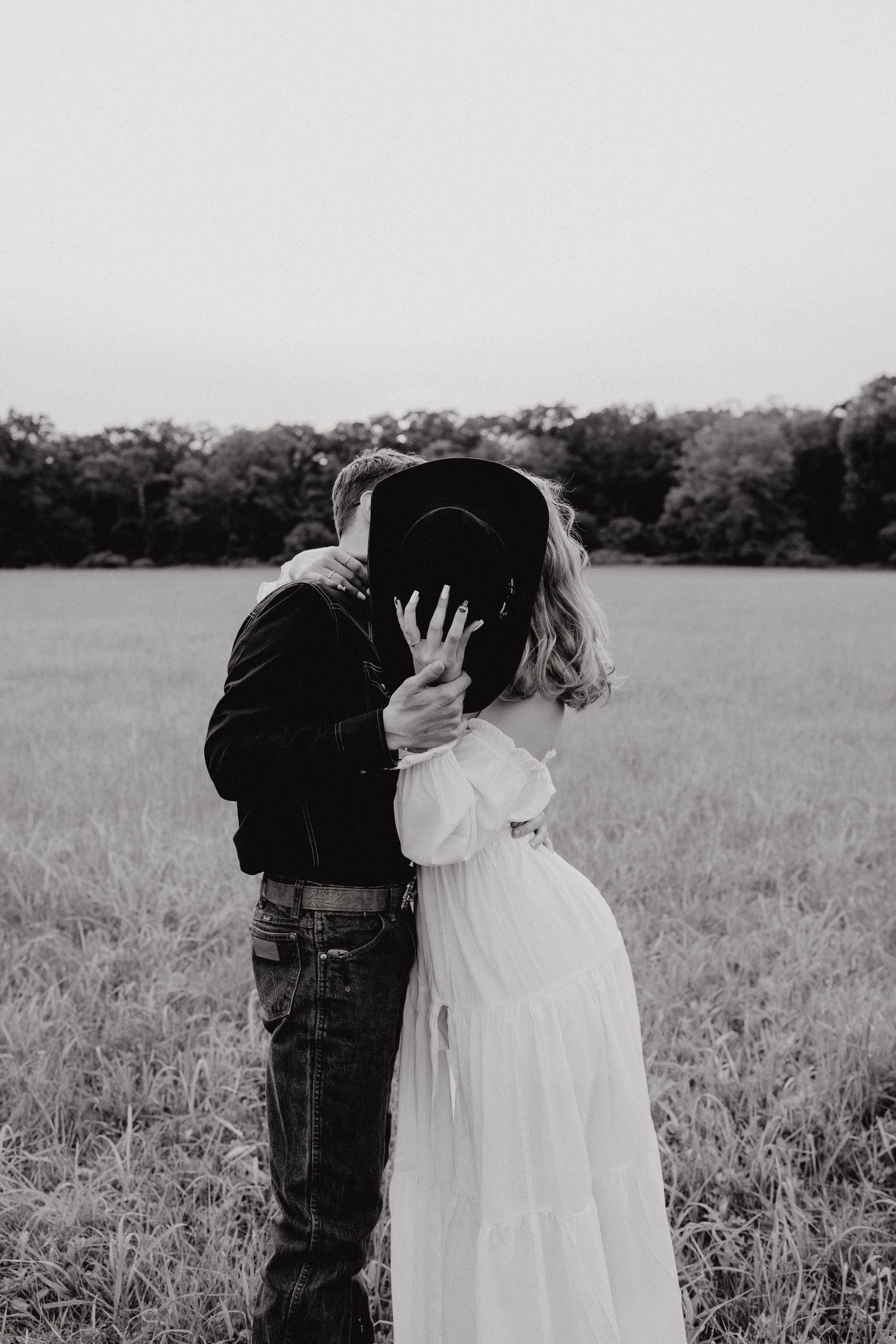 A romantic black and white photo of a couple embracing in a meadow.